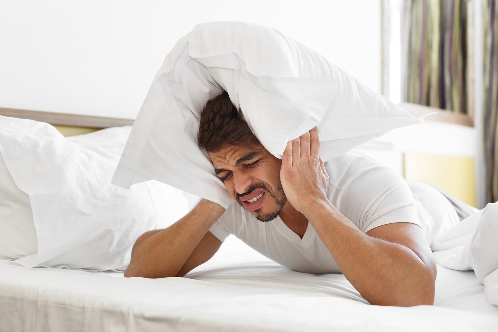 Sad man in bed covering head with pillow